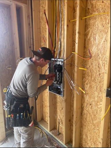 Electrician installing wiring and panel in wood-framed wall